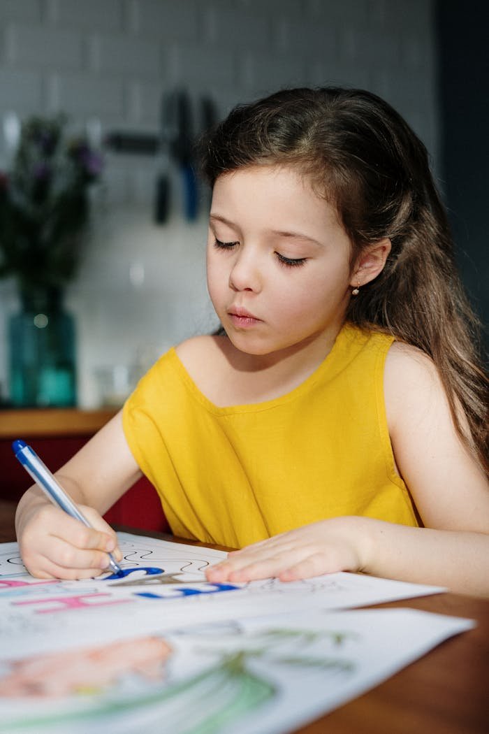A young girl focuses on drawing with a blue marker at home, enhancing creativity.